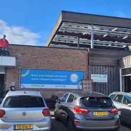 Voorgevel van kringloopwinkel met blauwe banner, parkeerplaatsen en moderne uitbouw