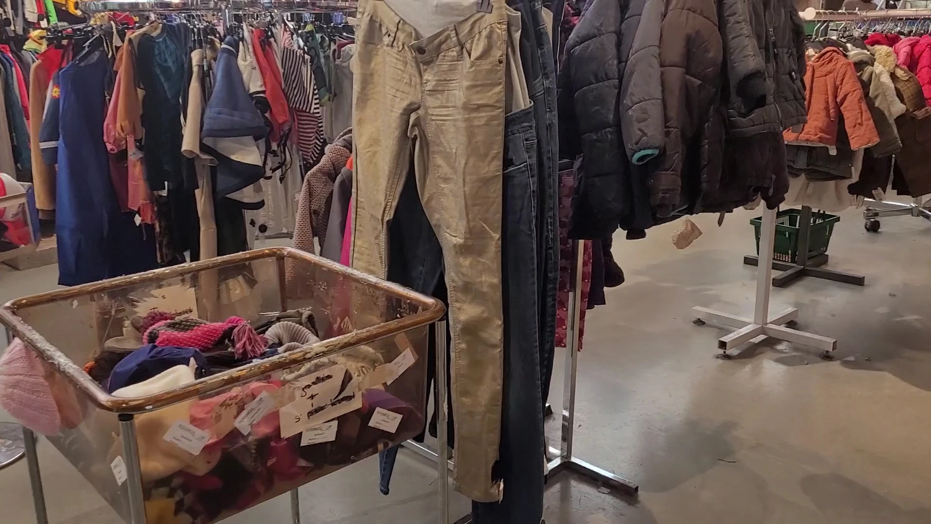 Tweedehands kleding op hangers en in bakken, met jassen, broeken en andere kledingstukken in verschillende kleuren