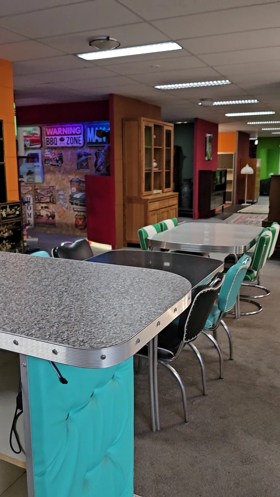 Interieur van kringloopwinkel met grijze en zwarte tafels met turkooizen stoelen, kleurrijke wanden op achtergrond
