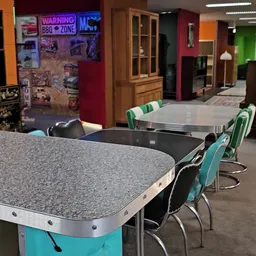 Interieur van kringloopwinkel met grijze en zwarte tafels met turkooizen stoelen, kleurrijke wanden op achtergrond