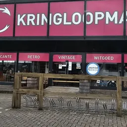 Gevel van Kringloopmania met roze uithangbord en houten terras ervoor met verschillende categorieën
