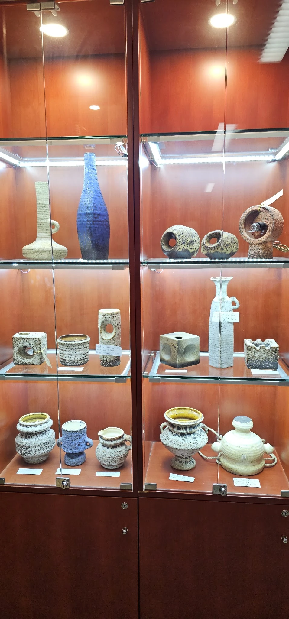 Vitrinekast met diverse kunstobjecten en keramische stukken met gaten, waaronder vazen en sculpturen
