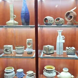 Vitrinekast met diverse kunstobjecten en keramische stukken met gaten, waaronder vazen en sculpturen