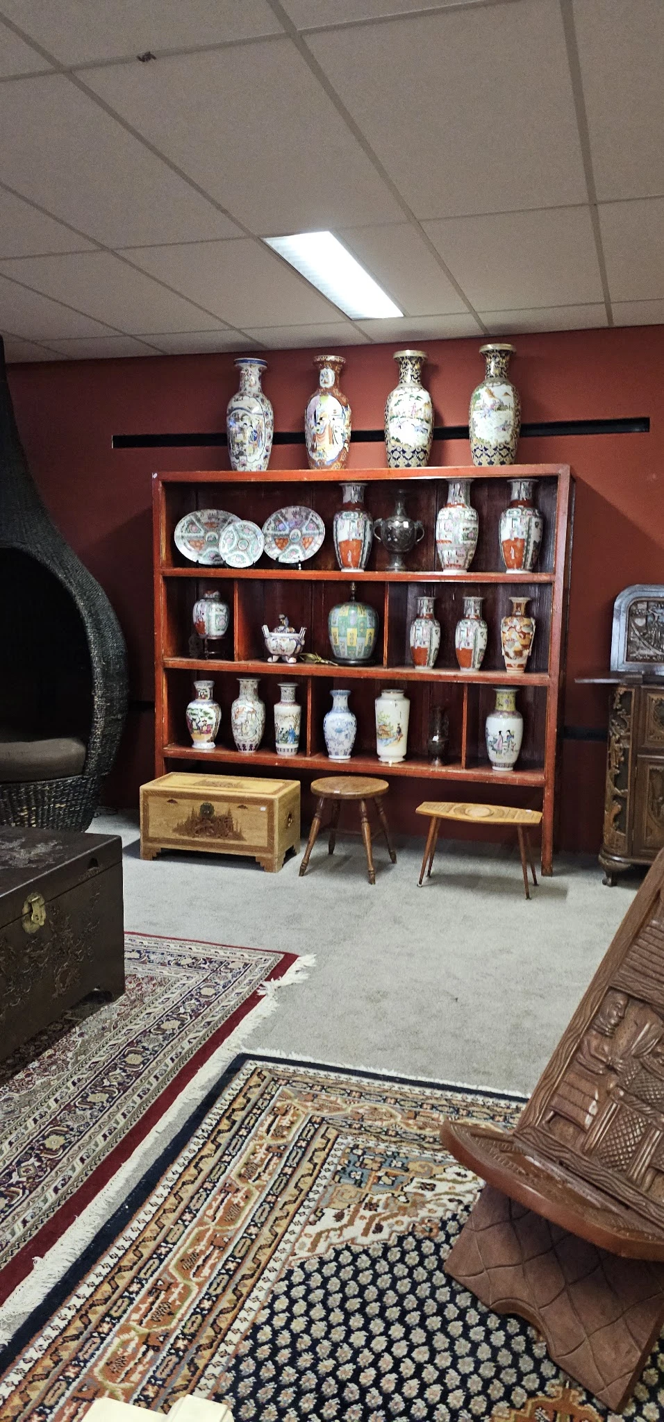 Houten vitrinekast met Aziatische porseleinen vazen, borden en decoratieve items, omgeven door houten meubels