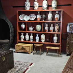 Houten vitrinekast met Aziatische porseleinen vazen, borden en decoratieve items, omgeven door houten meubels