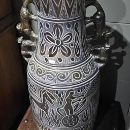Close-up van een decoratieve vaas met wit en zwart reliëfwerk en dierenfiguren als hengsels