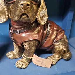 Close-up van een goudkleurig knuffelbeestje met bruinen jasje en halsband, met prijskaartje