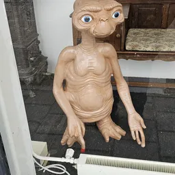 Houten sculptuur van een mannelijk figuur met anatomische details, zittend in een kringloopwinkel