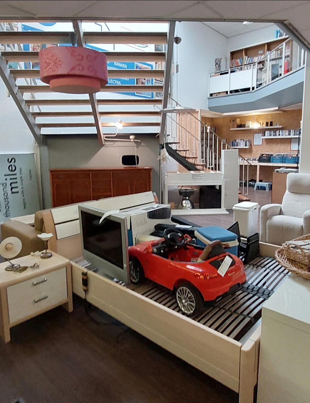Ruime winkelruimte met meubels, boeken, een rode speelgoedauto en trap naar bovenetage