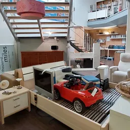 Ruime winkelruimte met meubels, boeken, een rode speelgoedauto en trap naar bovenetage