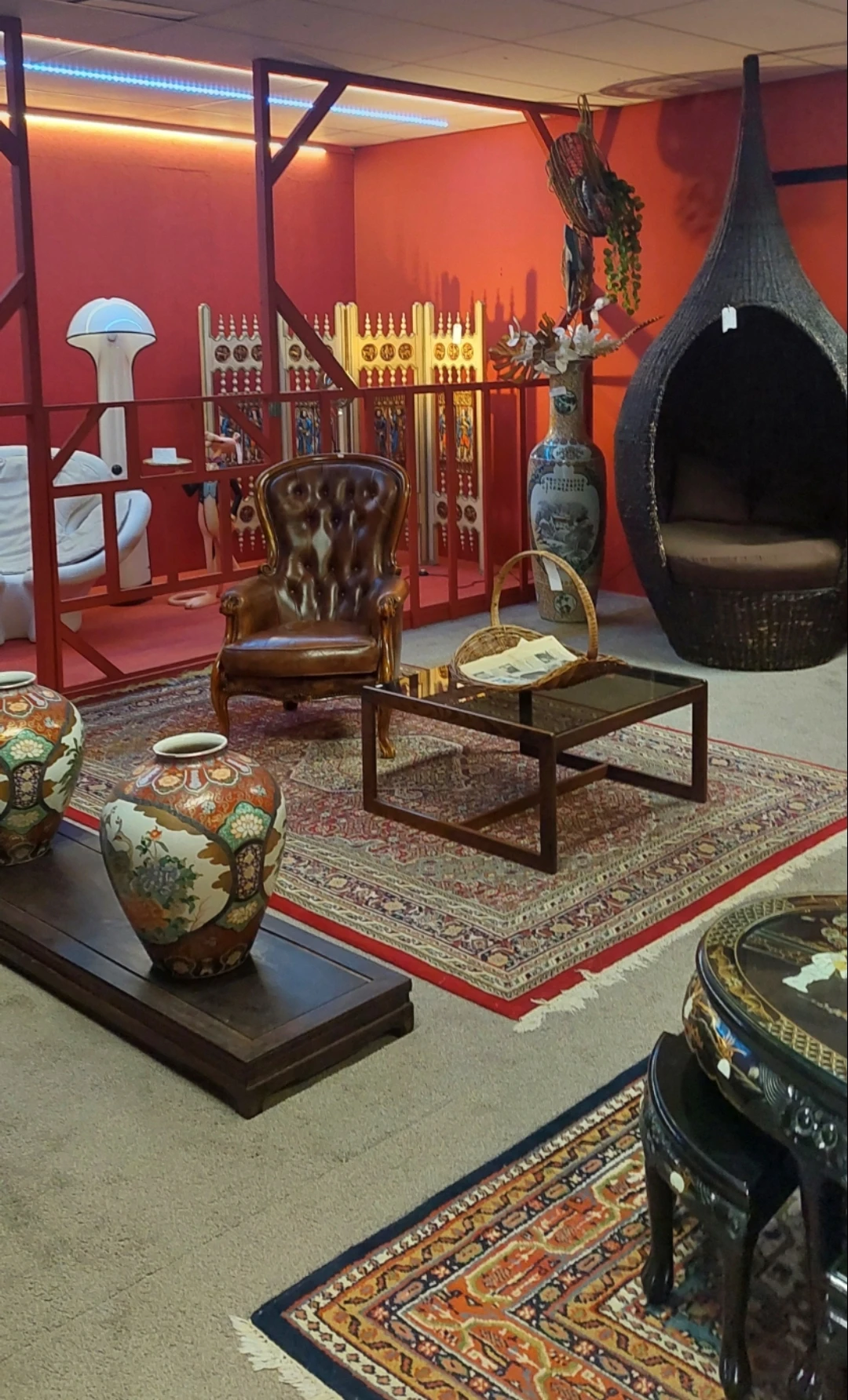 Winkelinterieur met bruine lederen fauteuil, salontafel, Aziatische decorstukken en rode vloerbedekking