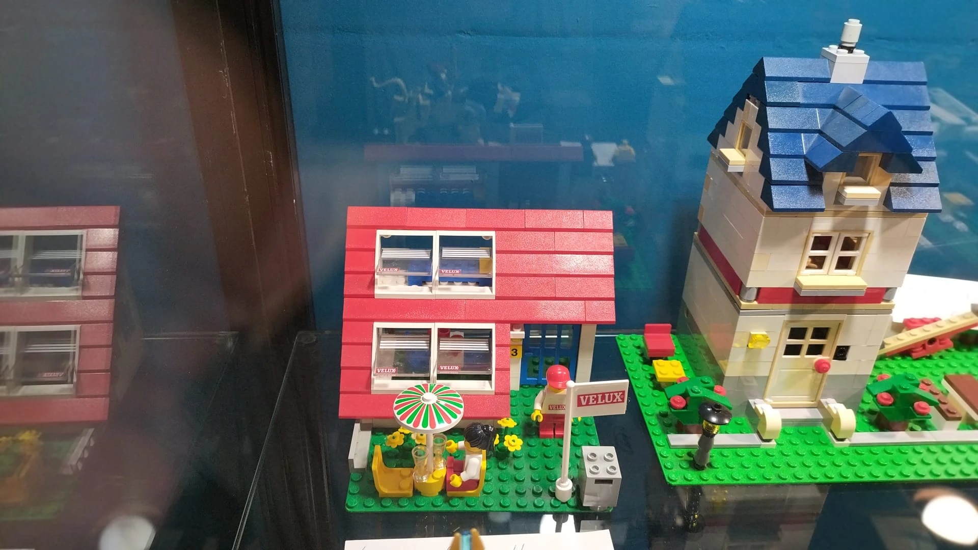 LEGO-huisjes in een display, waaronder een rood huis met groene tuin en accessoires