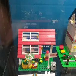 LEGO-huisjes in een display, waaronder een rood huis met groene tuin en accessoires