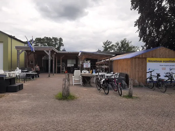 Exterieur van kringloopwinkel met houten gebouwen, fietsenstalling en parkeerplein
