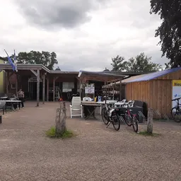 Exterieur van kringloopwinkel met houten gebouwen, fietsenstalling en parkeerplein