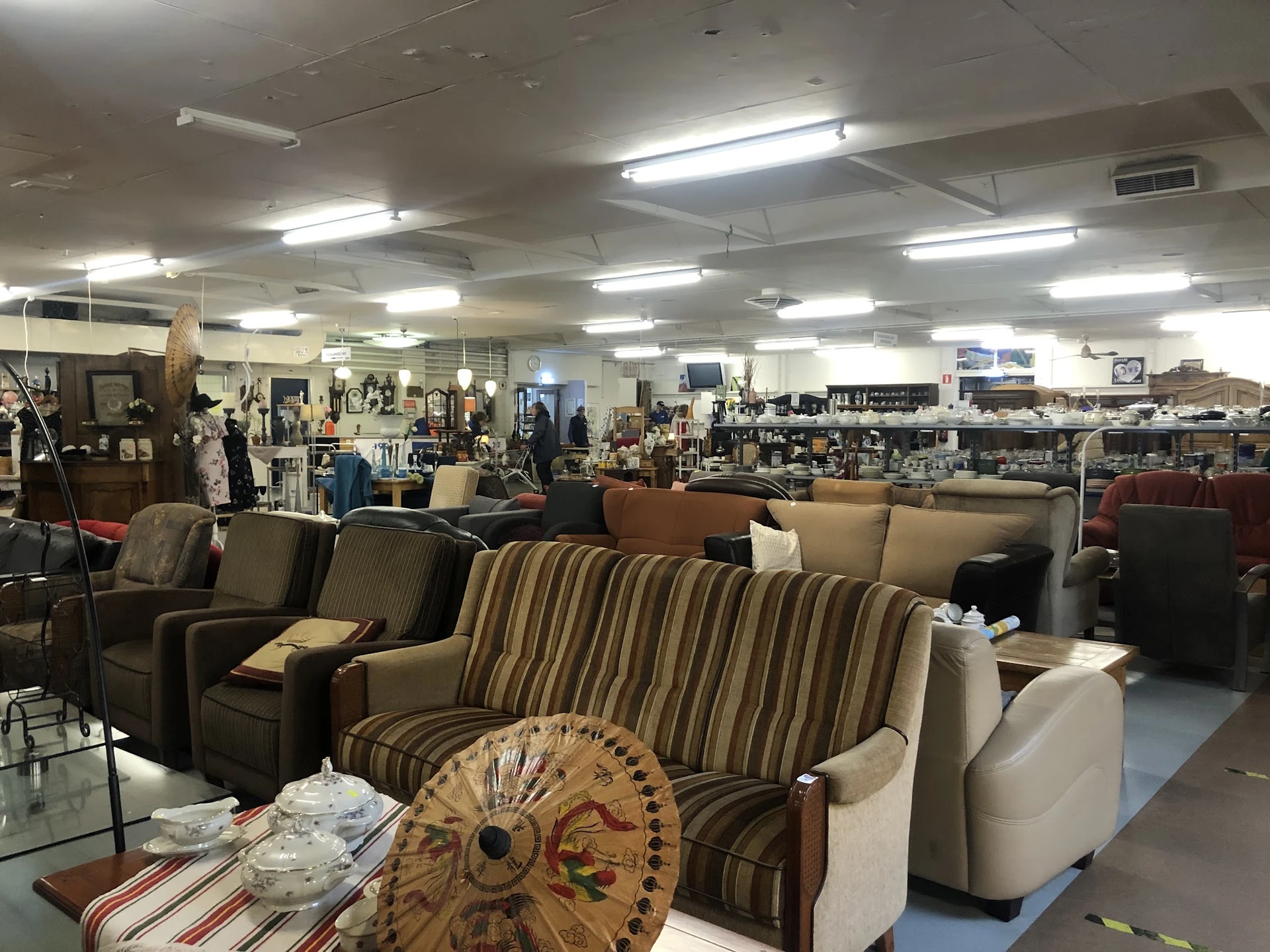 Uitgestalde meubels in de kringloopwinkel, waaronder gestreepte banken, fauteuils en decoratieve items