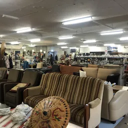 Uitgestalde meubels in de kringloopwinkel, waaronder gestreepte banken, fauteuils en decoratieve items