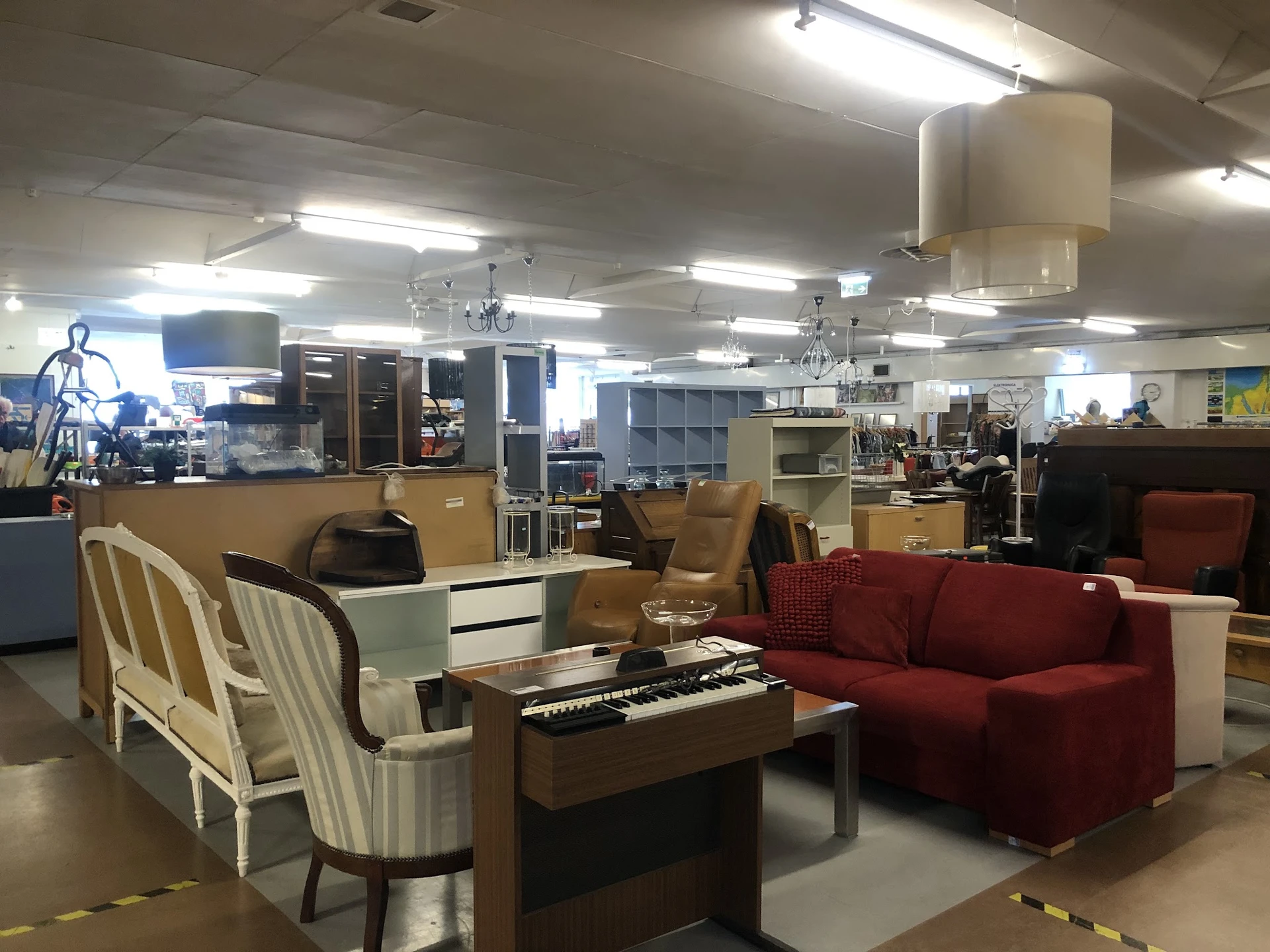 Winkelvloer met meubels: rode fauteuil, witte fauteuil, keyboard en diverse kasten en stellingen op de achtergrond