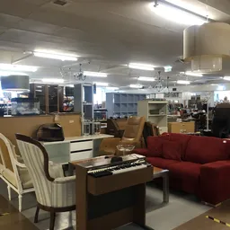 Winkelvloer met meubels: rode fauteuil, witte fauteuil, keyboard en diverse kasten en stellingen op de achtergrond
