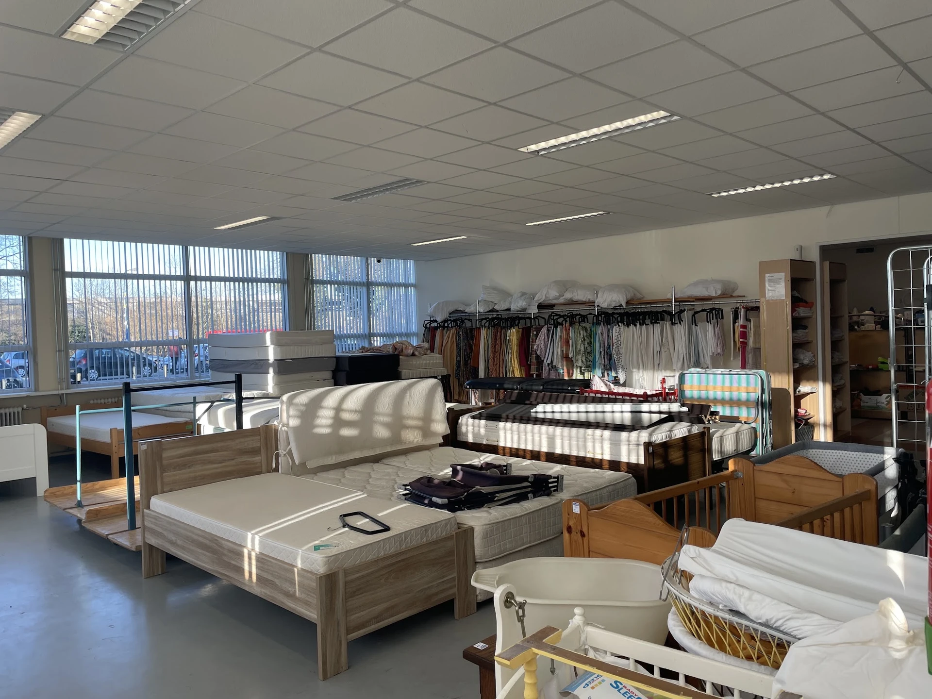 Interieur van kringloopwinkel met bedden, meubels, kleding op rekken en huishoudelijke artikelen