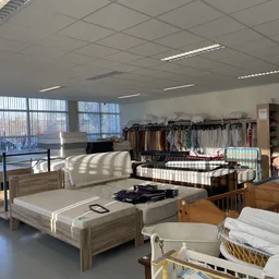 Interieur van kringloopwinkel met bedden, meubels, kleding op rekken en huishoudelijke artikelen