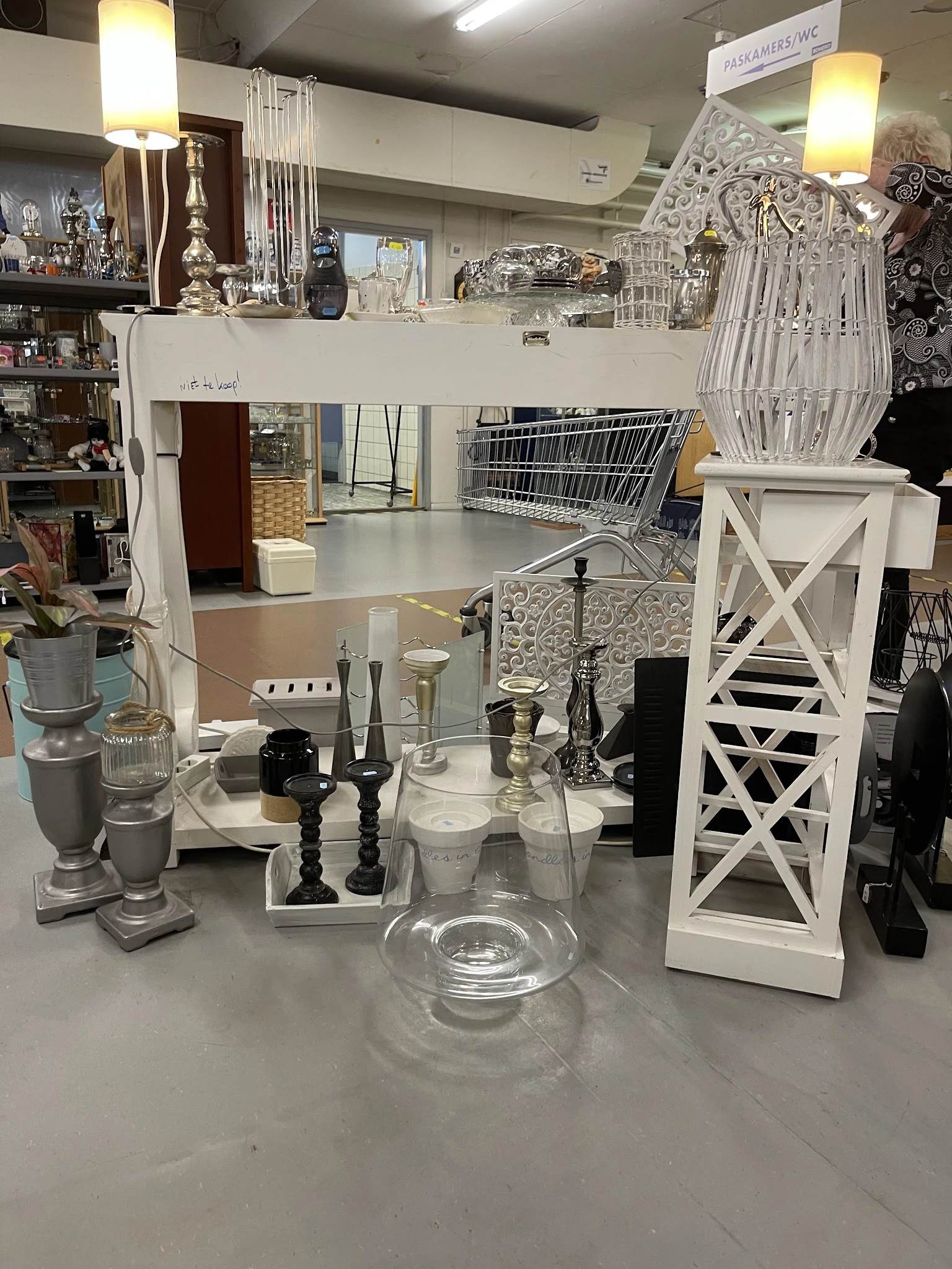 Tafeltje met decoratieve items: kandelaars, vazen, glazen objecten en witte houten sieraden in een kringloopwinkel