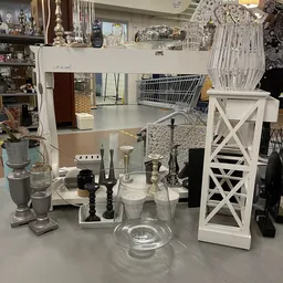 Tafeltje met decoratieve items: kandelaars, vazen, glazen objecten en witte houten sieraden in een kringloopwinkel