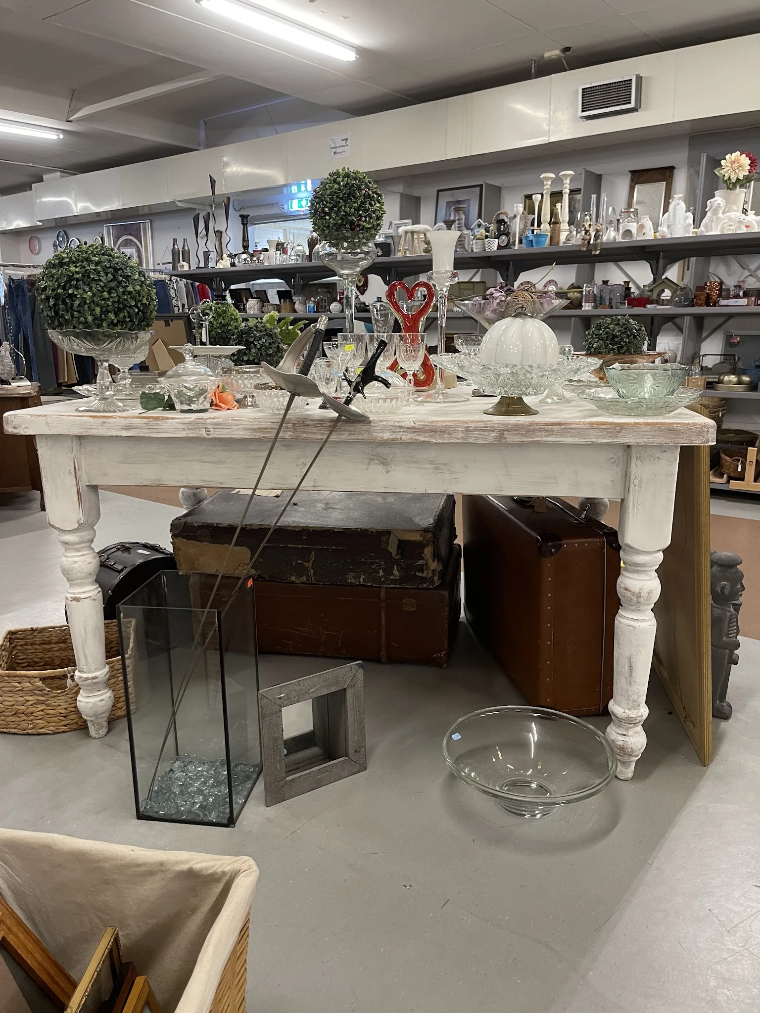 Witte tuintafel met diverse huishoudelijke artikelen en decoraties zoals glazen beelden, plantenpotten en kandelaars
