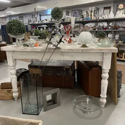 Witte tuintafel met diverse huishoudelijke artikelen en decoraties zoals glazen beelden, plantenpotten en kandelaars