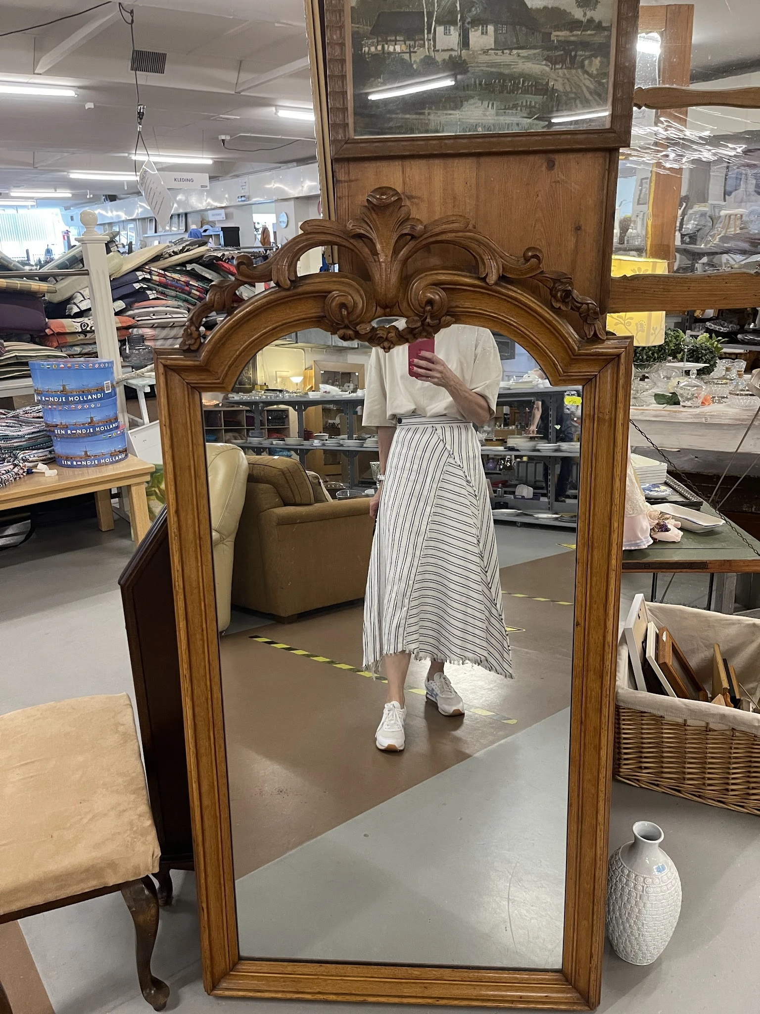 Grote houten spiegel met ornamentale lijst en decoratief figuur erin in winkelruimte