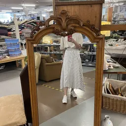 Grote houten spiegel met ornamentale lijst en decoratief figuur erin in winkelruimte