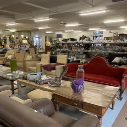 Winkelvloer met uitgestalde meubels: rode samt bank, beige stoelen, houten tafels en diverse spullen in het zicht