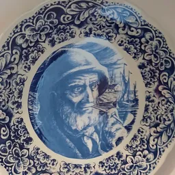 Decoratief blauw-wit porseleinbord met randversiering en portret van een bebaarde man in het centrum