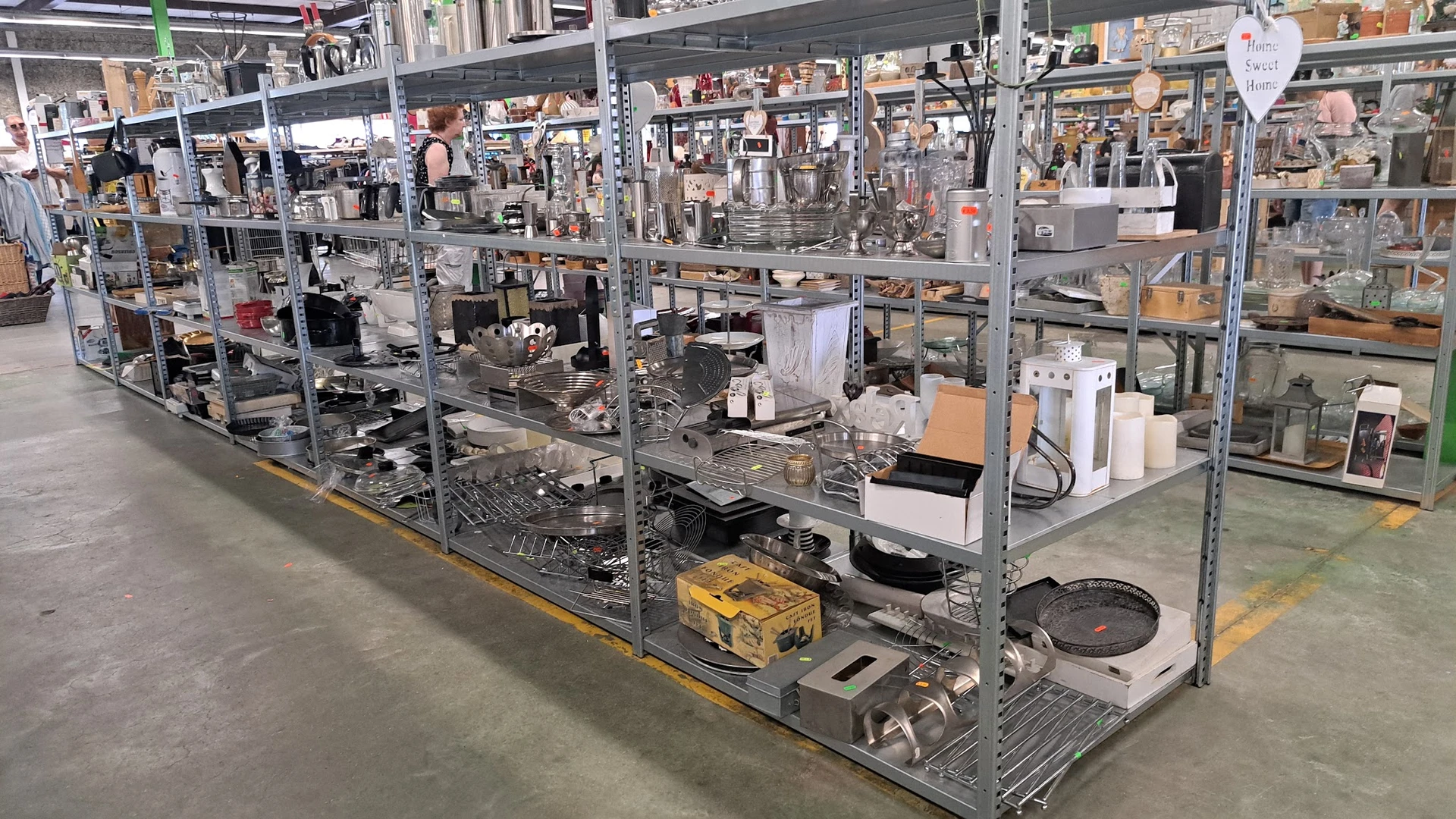 Metalen stellingen met verzameling huishoudelijke spullen, pannen, servies en apparaten in een kringloopwinkel