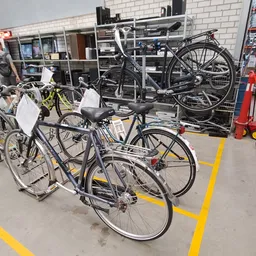 Tweedehands fietsen uitgestald in de winkel, met gele markeringen op de vloer