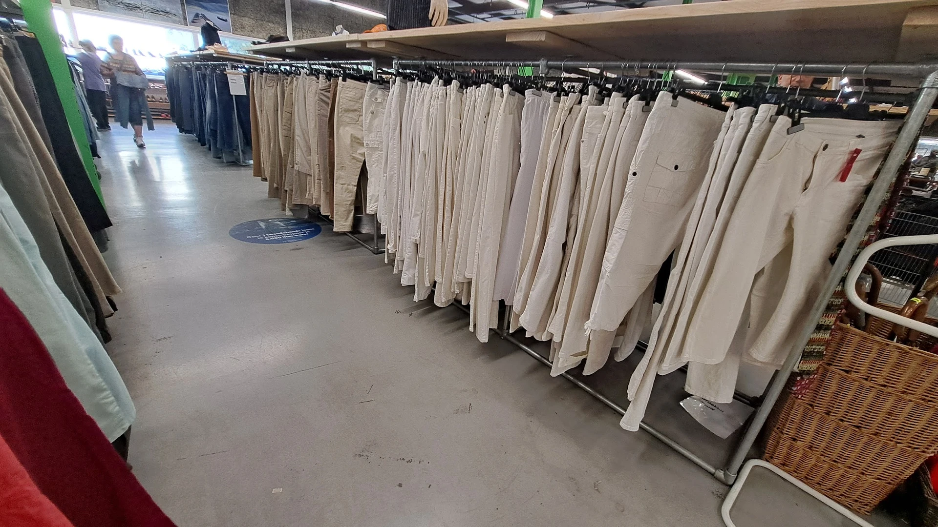 Rekken met tweedehands kleding in beige en witte tinten, opgehangen op winkelrekken