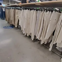 Rekken met tweedehands kleding in beige en witte tinten, opgehangen op winkelrekken