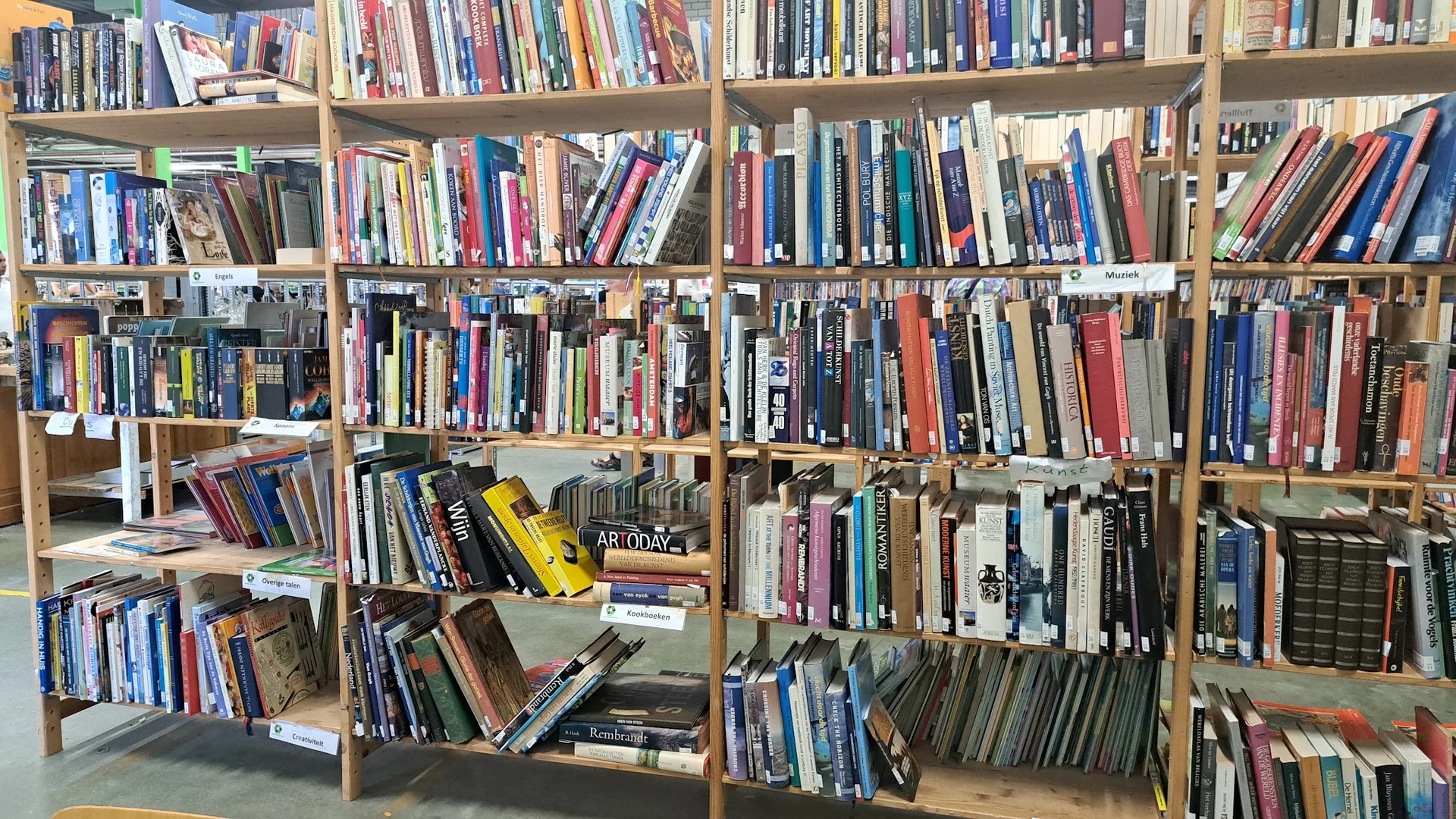 Houten stellingen vol met tweedehands cd's, dvd's en boeken in een kringloopwinkel