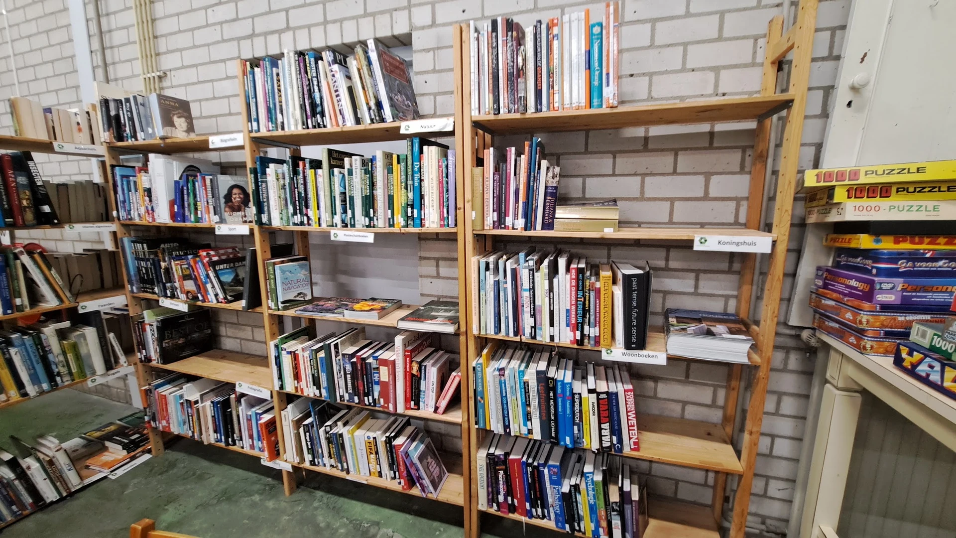 Houten boekenkasten tegen een bakstenen muur gevuld met tweedehands boeken en dvd's