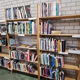 Houten boekenkasten tegen een bakstenen muur gevuld met tweedehands boeken en dvd's