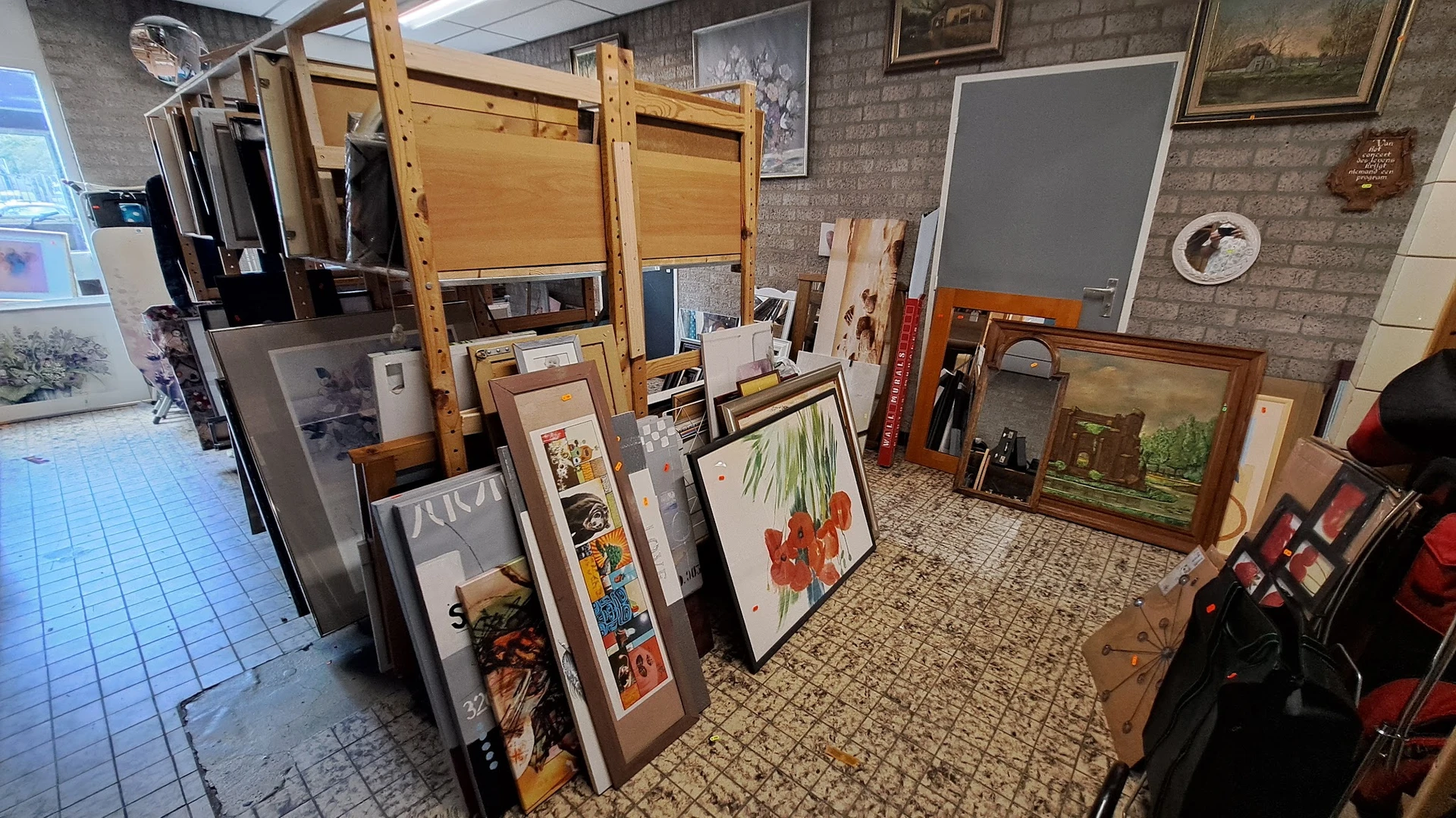 Diverse gebruikte artikelen zoals kunstwerken in lijsten, houten stellingen en huishoudartikelen uitgestald in de winkel