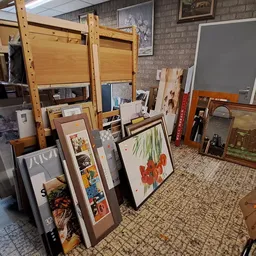 Diverse gebruikte artikelen zoals kunstwerken in lijsten, houten stellingen en huishoudartikelen uitgestald in de winkel