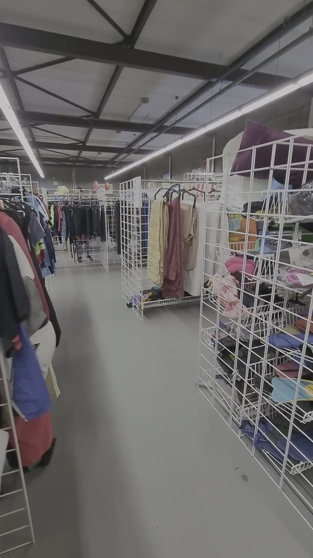 Interieur van kringloopwinkel met witte stellingen vol kleding en textiel