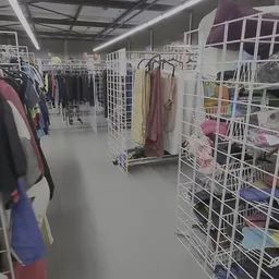 Interieur van kringloopwinkel met witte stellingen vol kleding en textiel