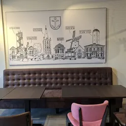 Zithoek met bruine gestoffeerde bank en roze stoelen aan zwarte tafels, onder decoratieve wandtekening van stadsgezicht