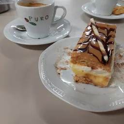 Stuk gebak met chocolade topping en koffiekopje op terras