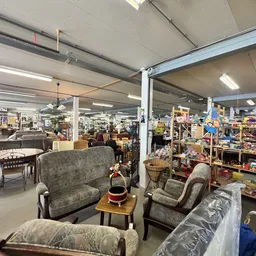 Winkelvloer met gebruikte meubels, stoelen en fauteuils, stellingen met diverse artikelen op de achtergrond