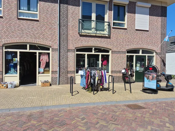 Bakstenen gevel van kringloopwinkel met drie etalages, kleding op rekken buiten uitgestald