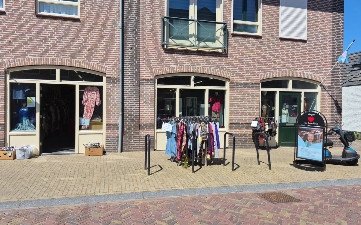 Bakstenen gevel van kringloopwinkel met drie etalages, kleding op rekken buiten uitgestald