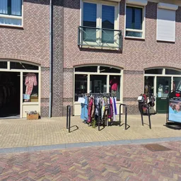 Bakstenen gevel van kringloopwinkel met drie etalages, kleding op rekken buiten uitgestald